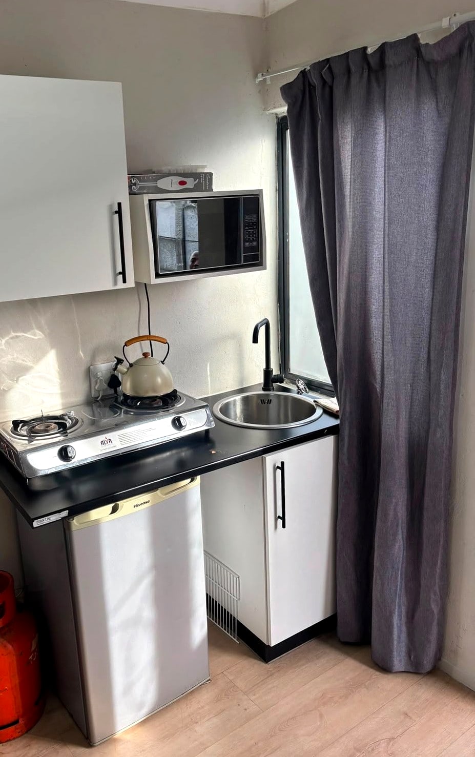 A 12B kitchenette: gas stove, kettle, microwave, sink and bar fridge