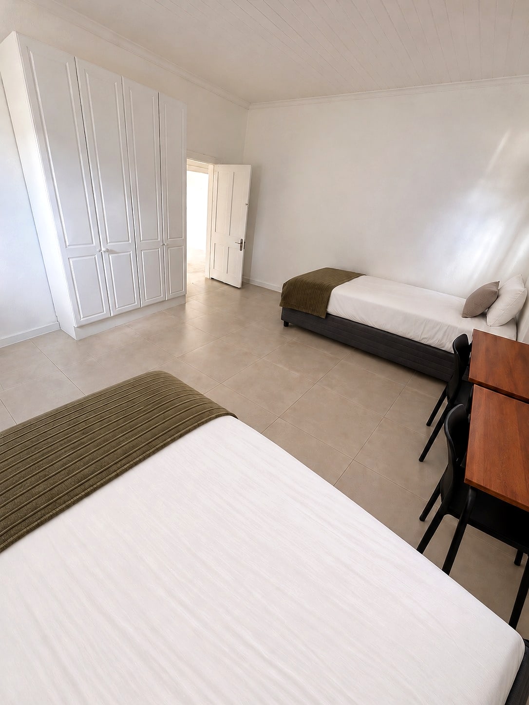 A Caledon sharing room: a made bed beside a desk, with a built-in wardrobe