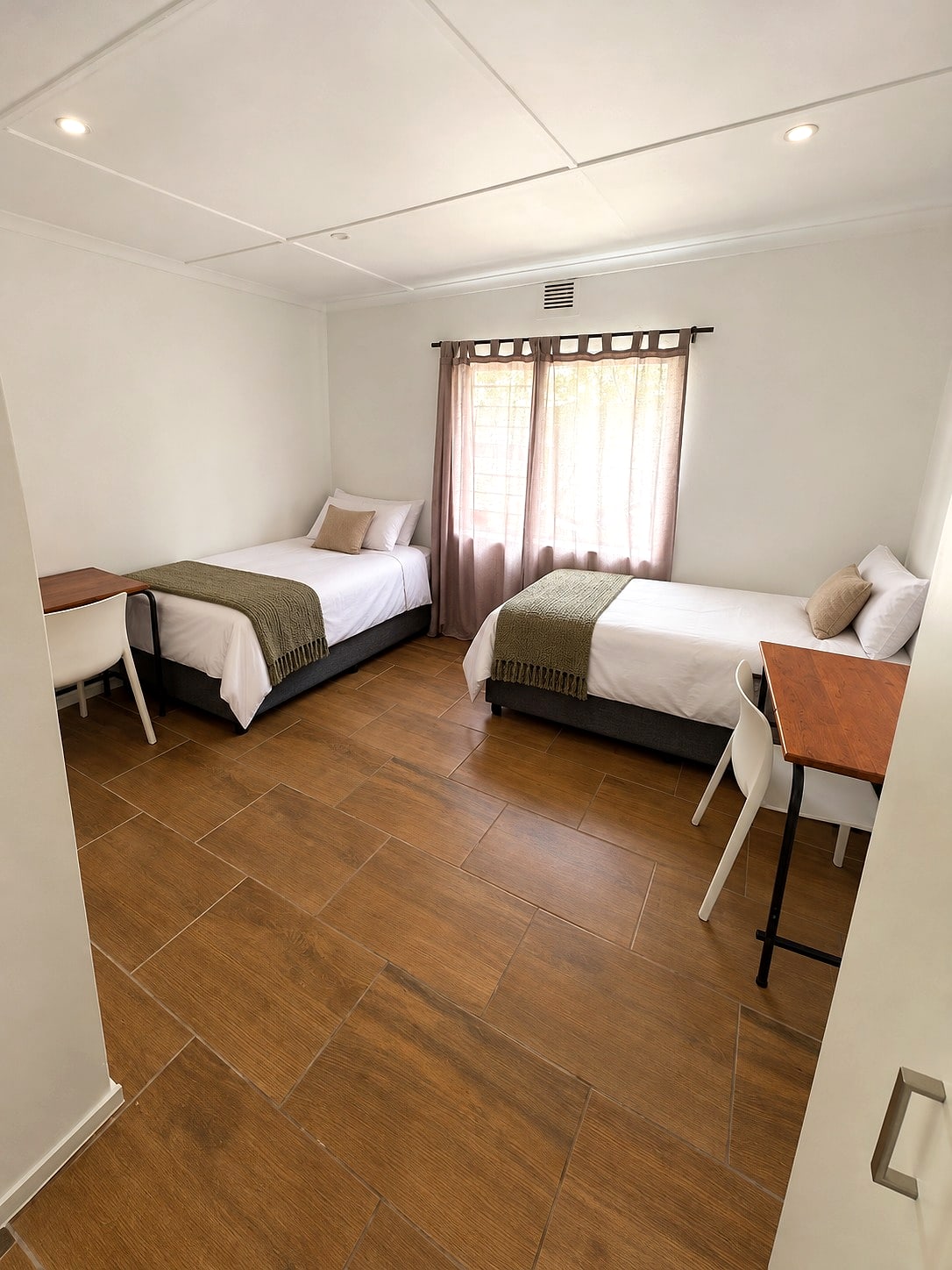 A Caledon sharing room with two made beds, a desk and a wood-look floor