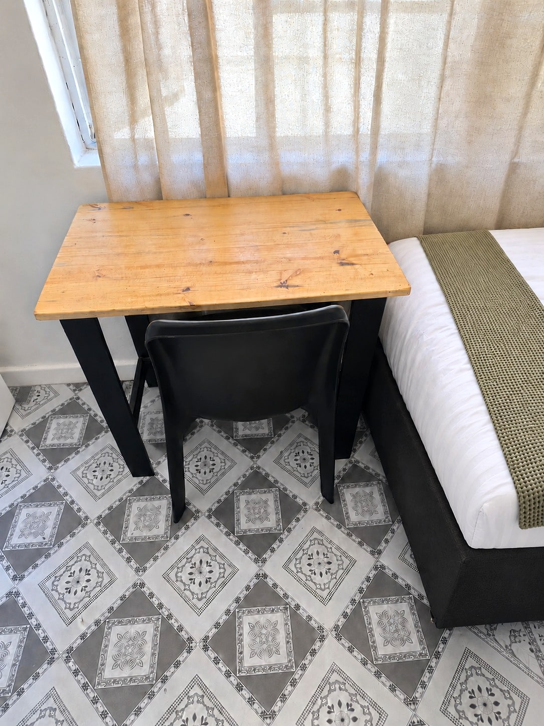 A study desk and chair beside a made bed at Inspan