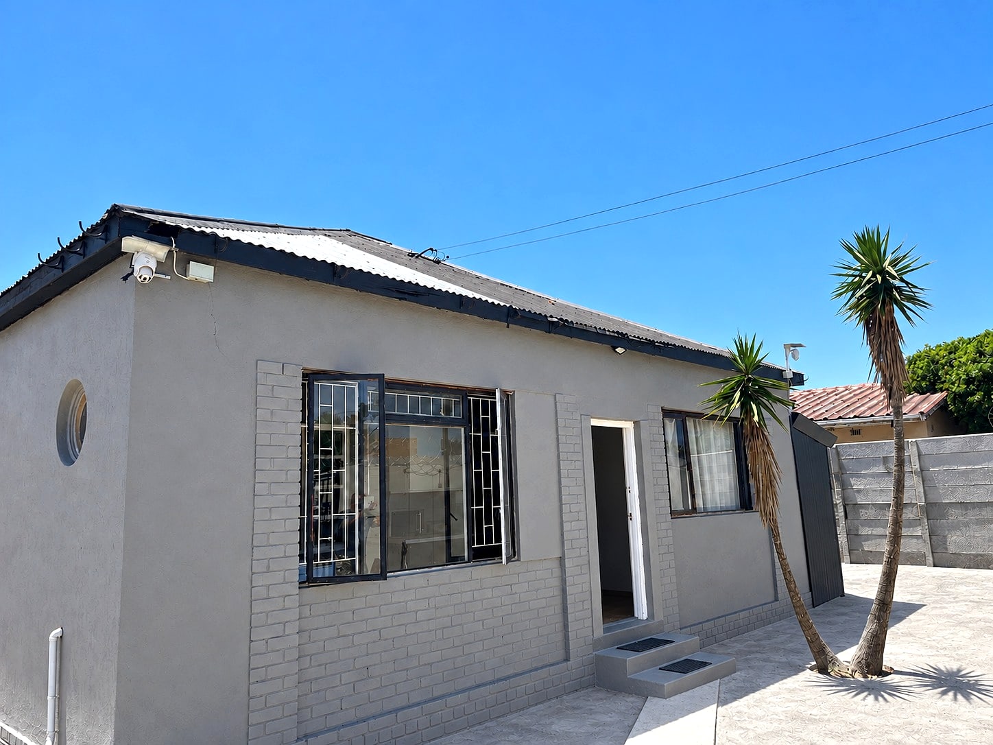Inspan Residence: a grey house with palm trees and a paved yard