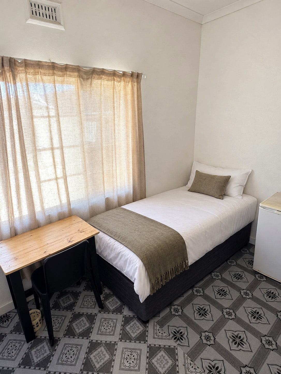 An Inspan room: a made single bed and a pine desk by the window