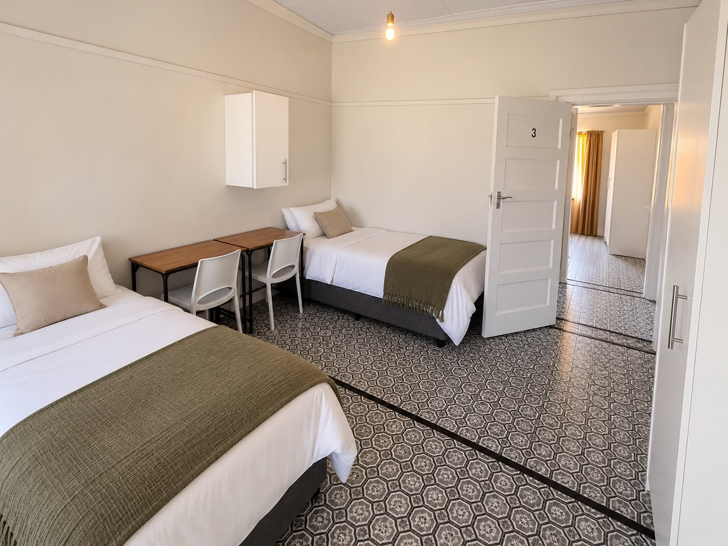 An Inspan sharing room: two made beds and two desks on patterned tiles